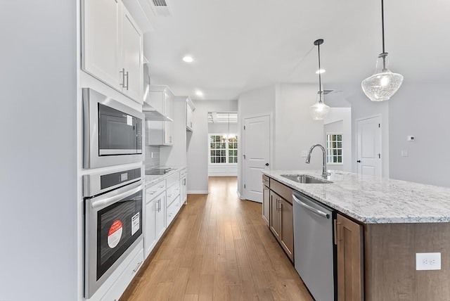 kitchen featuring stainless steel appliances, pendant lighting, a center island with sink, white cabinets, and light wood-type flooring