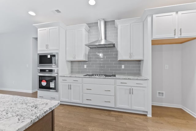 kitchen featuring white cabinetry, wall chimney range hood, backsplash, appliances with stainless steel finishes, and light wood-type flooring