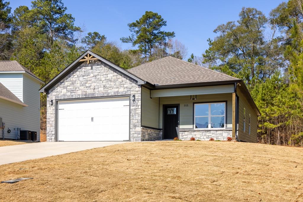 view of front of property featuring a shingled roof, central AC, a front yard, a garage, and driveway