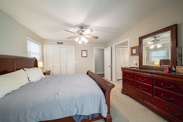 bedroom featuring light colored carpet, visible vents, two closets, and ceiling fan