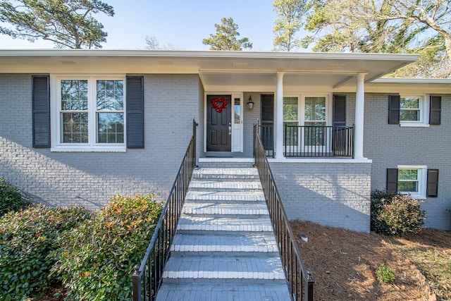 doorway to property featuring covered porch and brick siding