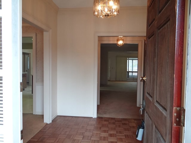 interior space featuring wallpapered walls, a notable chandelier, baseboards, and ornamental molding