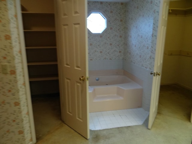 bathroom with wallpapered walls, a garden tub, and a walk in closet