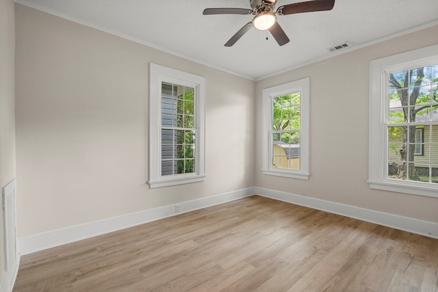 spare room with visible vents, a healthy amount of sunlight, crown molding, and light wood-style flooring