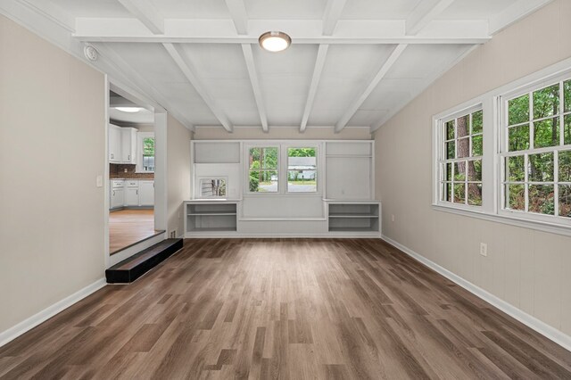 unfurnished living room with beam ceiling, baseboards, and wood finished floors