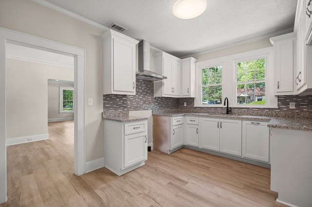 kitchen with light wood finished floors, a sink, wall chimney range hood, and tasteful backsplash