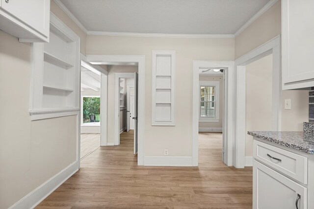 kitchen featuring baseboards, white cabinets, light wood-type flooring, and crown molding