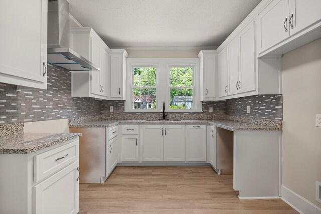 kitchen featuring light wood-style floors, a textured ceiling, backsplash, a sink, and wall chimney exhaust hood