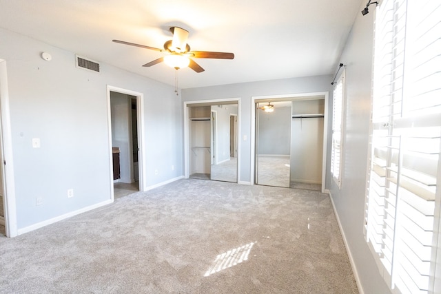 unfurnished bedroom with ceiling fan, ensuite bathroom, light carpet, and two closets