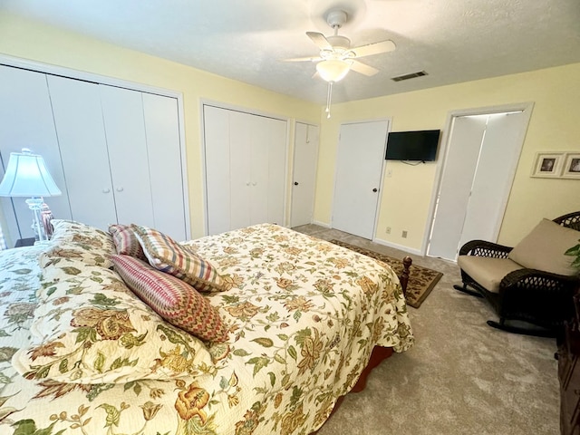 bedroom with light carpet, two closets, and ceiling fan