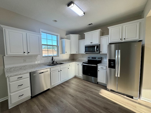 kitchen featuring sink, wood-type flooring, a textured ceiling, white cabinets, and appliances with stainless steel finishes