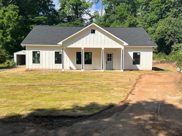 view of front of house featuring a shingled roof, board and batten siding, covered porch, and a front yard