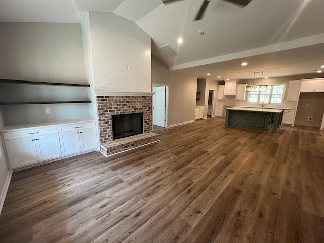 unfurnished living room with a brick fireplace, dark wood finished floors, a ceiling fan, baseboards, and lofted ceiling