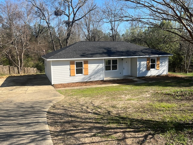 view of front of property featuring a shingled roof, concrete driveway, a front yard, and fence