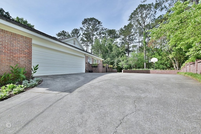 view of property exterior featuring fence, a garage, brick siding, and driveway