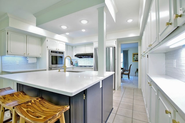 kitchen with light tile patterned floors, a sink, a kitchen breakfast bar, light countertops, and tasteful backsplash