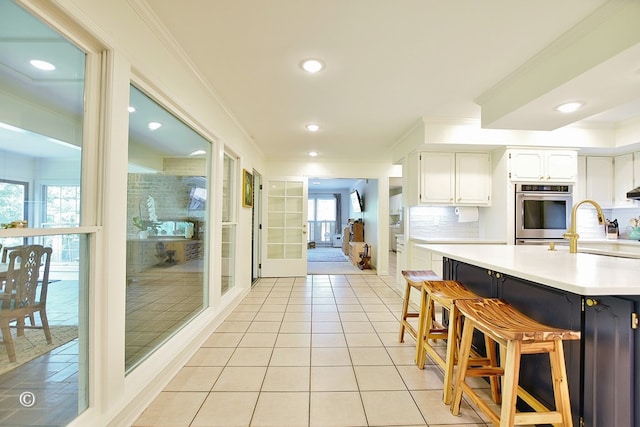 kitchen with tasteful backsplash, a sink, crown molding, light countertops, and white cabinets