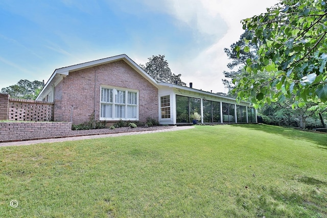 rear view of house with a yard, a sunroom, and brick siding