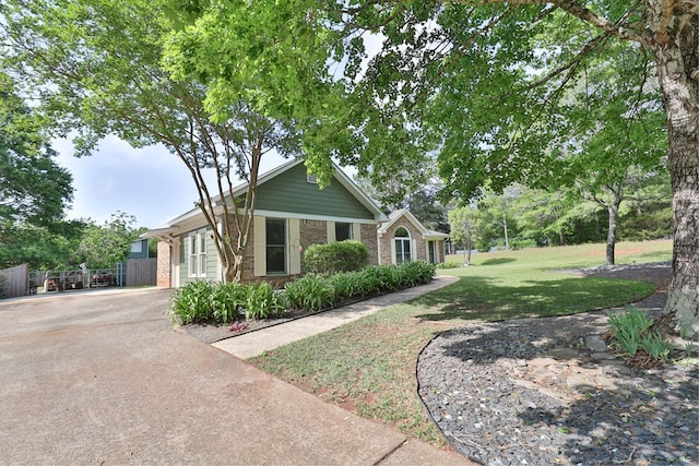ranch-style home featuring concrete driveway, brick siding, fence, and a front lawn