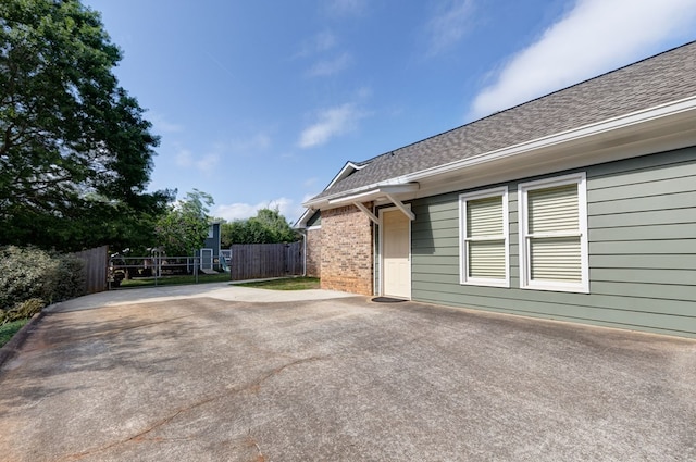 view of side of property with fence, a gate, a shingled roof, and brick siding