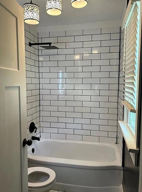 bathroom with tiled shower / bath combo and toilet