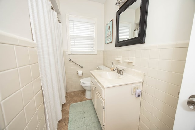 full bath with tile walls, toilet, wainscoting, vanity, and tile patterned floors