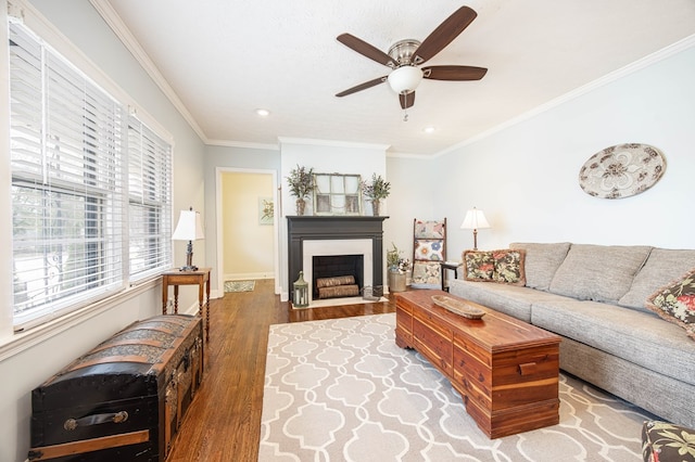 living room featuring baseboards, a ceiling fan, a fireplace with flush hearth, wood finished floors, and crown molding