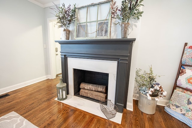 room details featuring baseboards, visible vents, a fireplace with flush hearth, ornamental molding, and wood finished floors