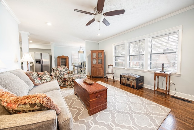 living area with crown molding, visible vents, ceiling fan, wood finished floors, and baseboards