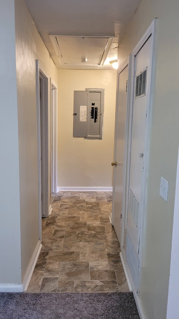 hall featuring electric panel, stone finish floor, attic access, and baseboards