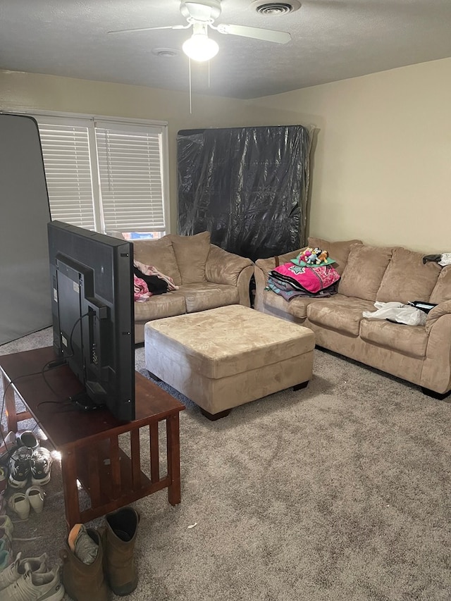 living room with a textured ceiling, visible vents, carpet floors, and ceiling fan