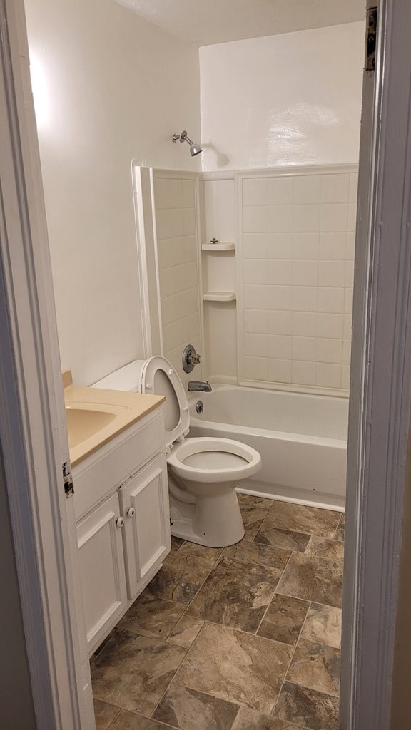 bathroom featuring toilet, stone finish flooring, vanity, and shower / bath combination