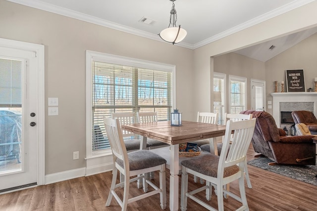 dining space with a fireplace, wood finished floors, visible vents, baseboards, and ornamental molding