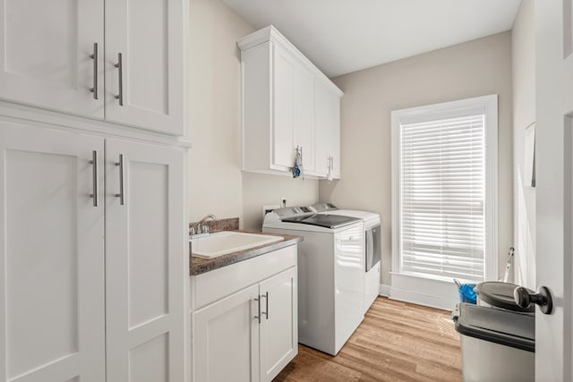 clothes washing area featuring separate washer and dryer, a sink, baseboards, cabinet space, and light wood finished floors