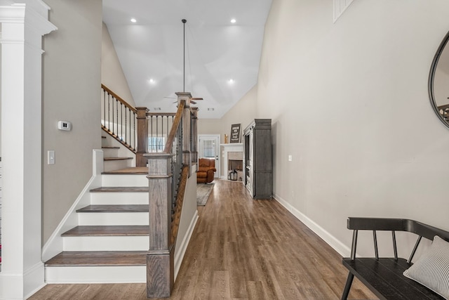 staircase with a ceiling fan, wood finished floors, ornate columns, a fireplace, and high vaulted ceiling