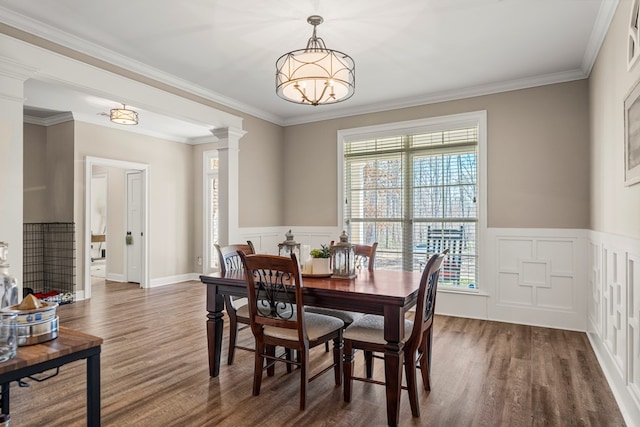 dining area featuring crown molding, a wainscoted wall, decorative columns, and wood finished floors