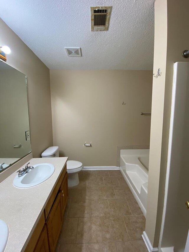 bathroom featuring a textured ceiling, vanity, toilet, and a tub to relax in