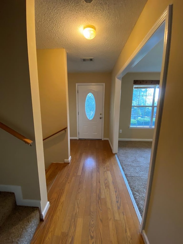 doorway to outside with a textured ceiling and light hardwood / wood-style flooring