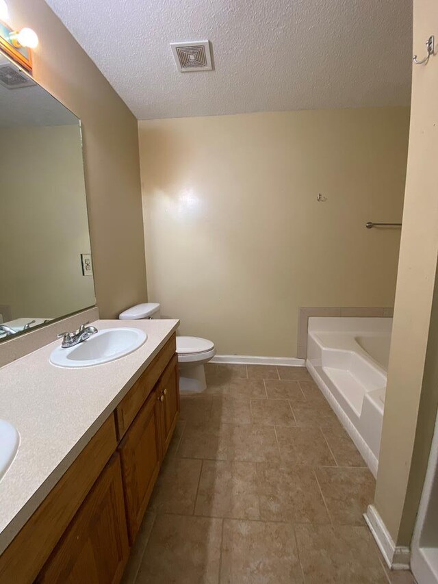 bathroom with vanity, tile patterned flooring, toilet, a textured ceiling, and a tub to relax in