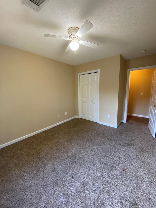 unfurnished bedroom featuring a textured ceiling, a closet, dark carpet, and ceiling fan