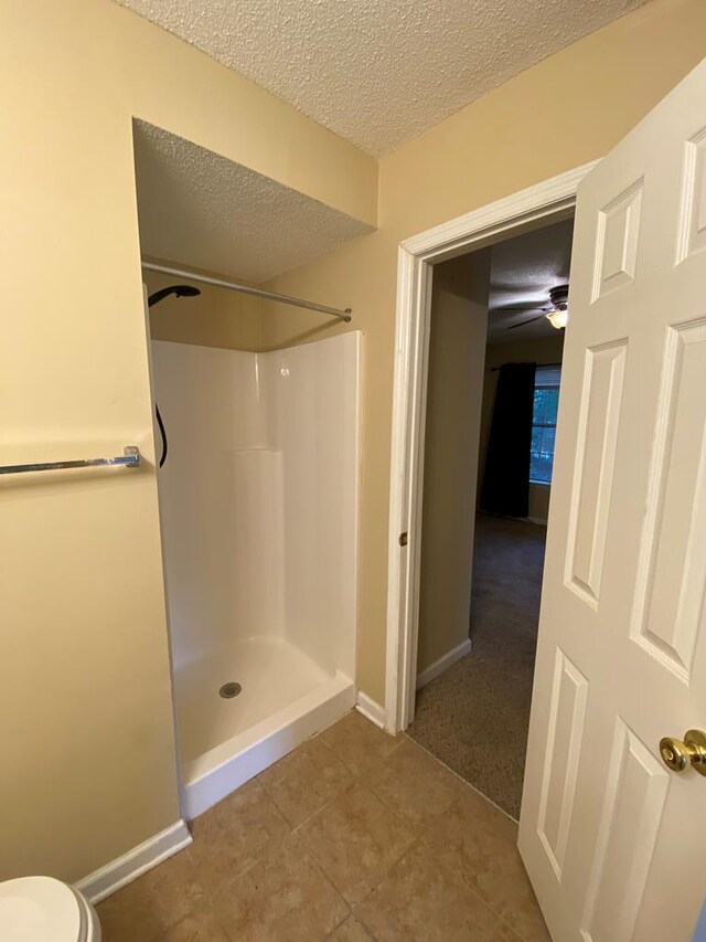 bathroom featuring a textured ceiling, tile patterned flooring, toilet, and walk in shower