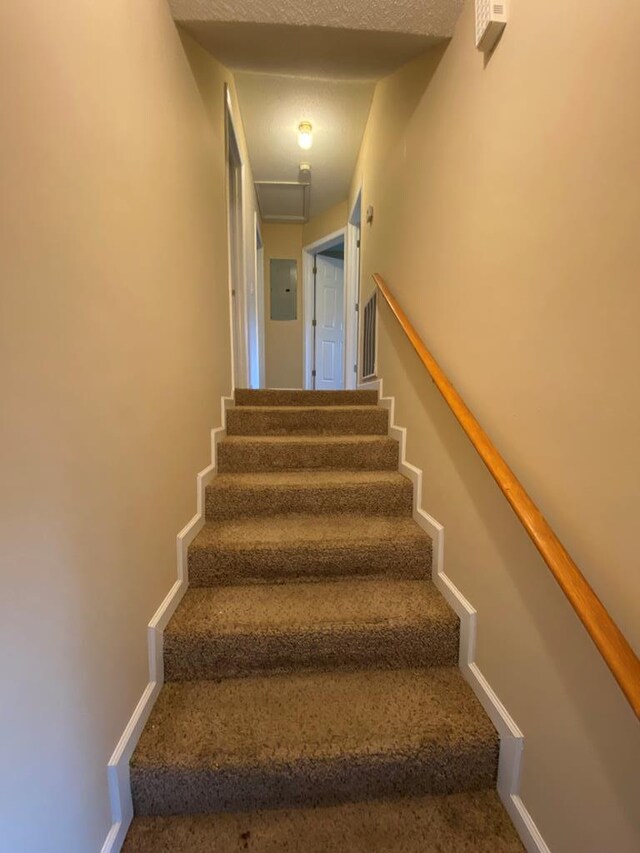 stairway with a textured ceiling and electric panel