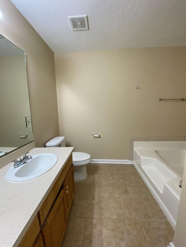 bathroom with a bathing tub, tile patterned flooring, a textured ceiling, toilet, and vanity