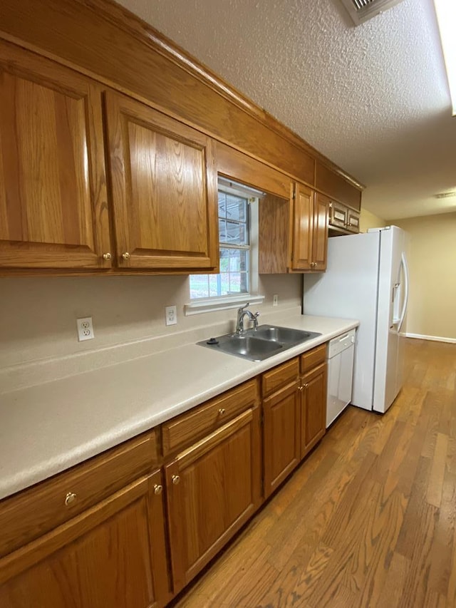 kitchen featuring sink, white dishwasher, a textured ceiling, and light wood-type flooring