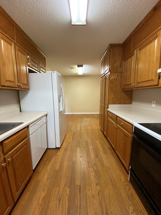 kitchen with a textured ceiling, sink, light hardwood / wood-style floors, and white appliances