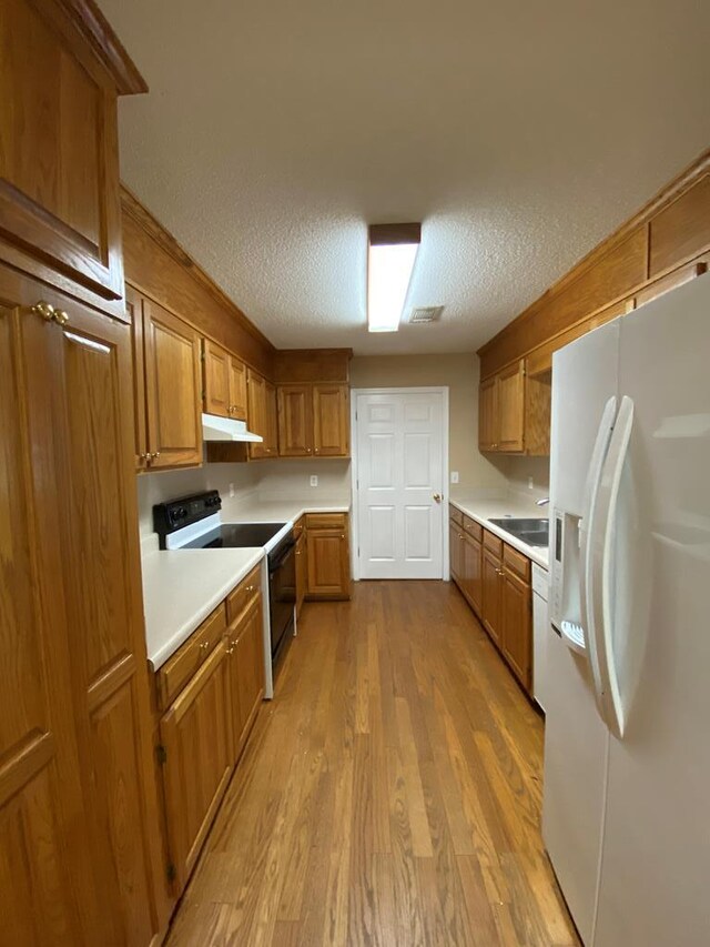 kitchen with a textured ceiling, sink, white appliances, and light wood-type flooring