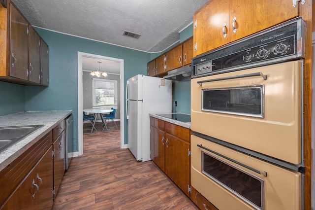 kitchen featuring white appliances, dark wood finished floors, under cabinet range hood, a chandelier, and a textured ceiling