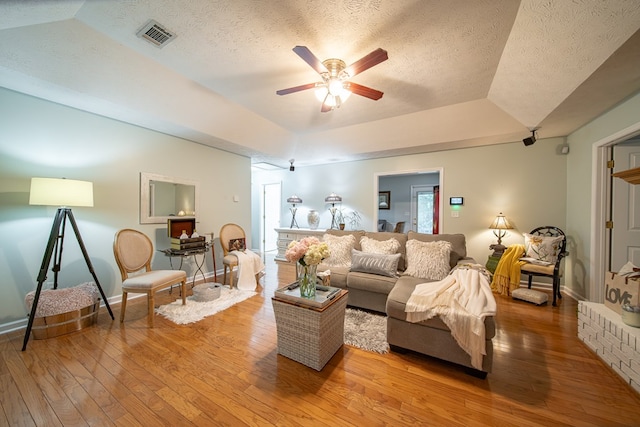 living room featuring ceiling fan, wood-type flooring, a raised ceiling, and a textured ceiling