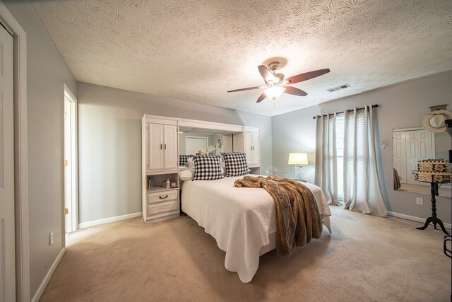 bedroom with ceiling fan, light carpet, and a textured ceiling