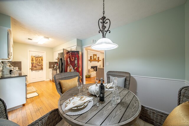 dining area featuring a fireplace, a textured ceiling, and light wood-type flooring